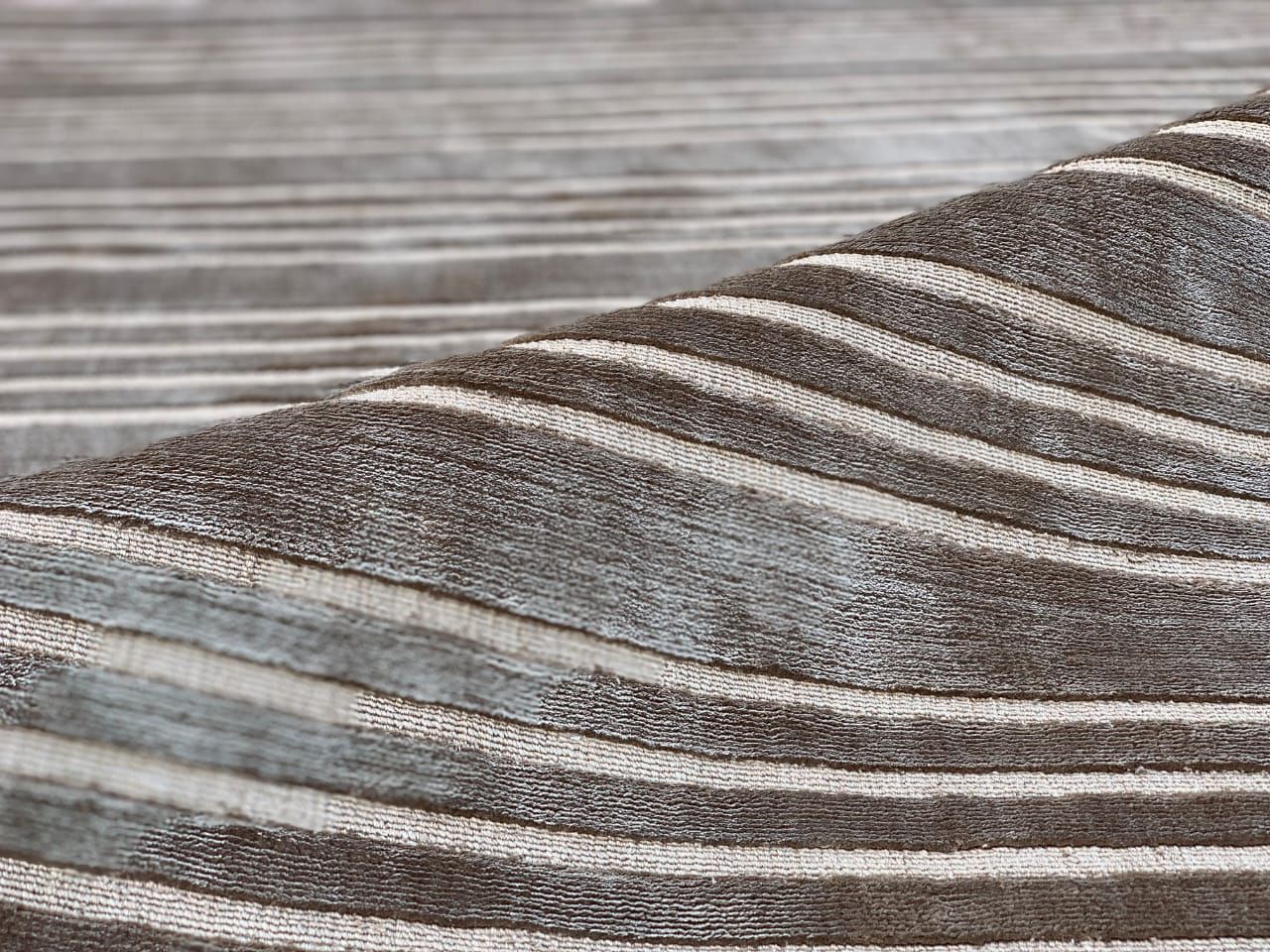 Rug with wavy stripes in taupe and ivory, folded to show the pile